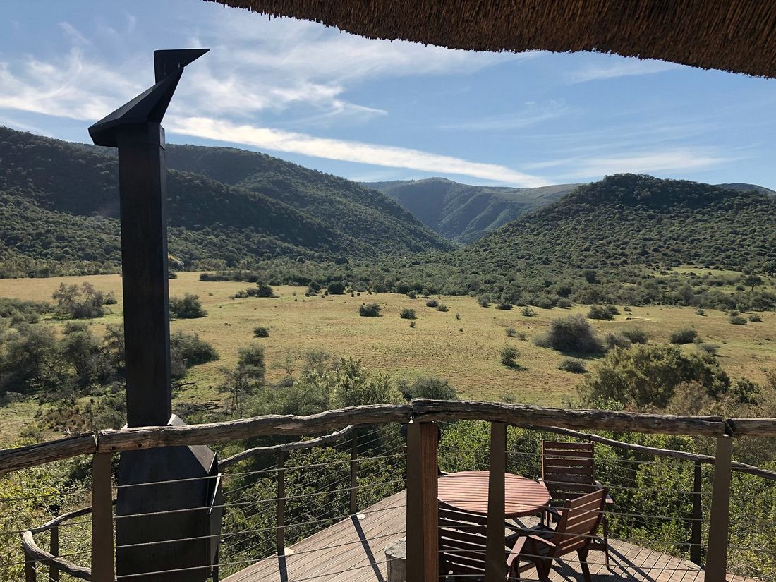 A thatched camp deck looking over open bushveld and green hills, Addo, South Africa